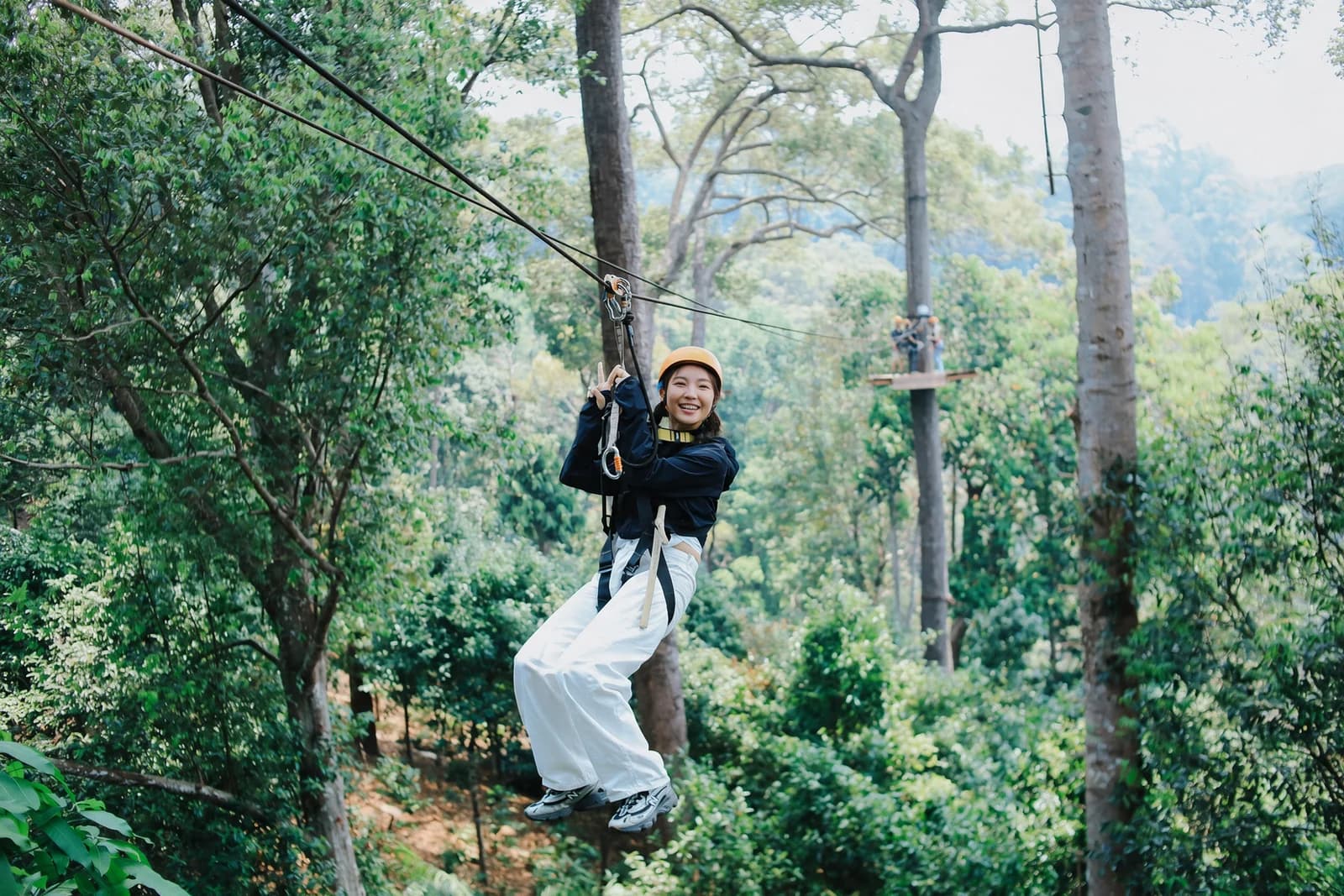 A zipline participant in white trousers and gray sneakers among forest trees
